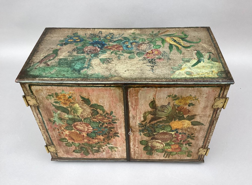 An eighteenth-century hand-painted wooden cabinet on a tall stand, featuring floral artwork across the twin doors, side panels, and apron, mounted with brass hinges. View X