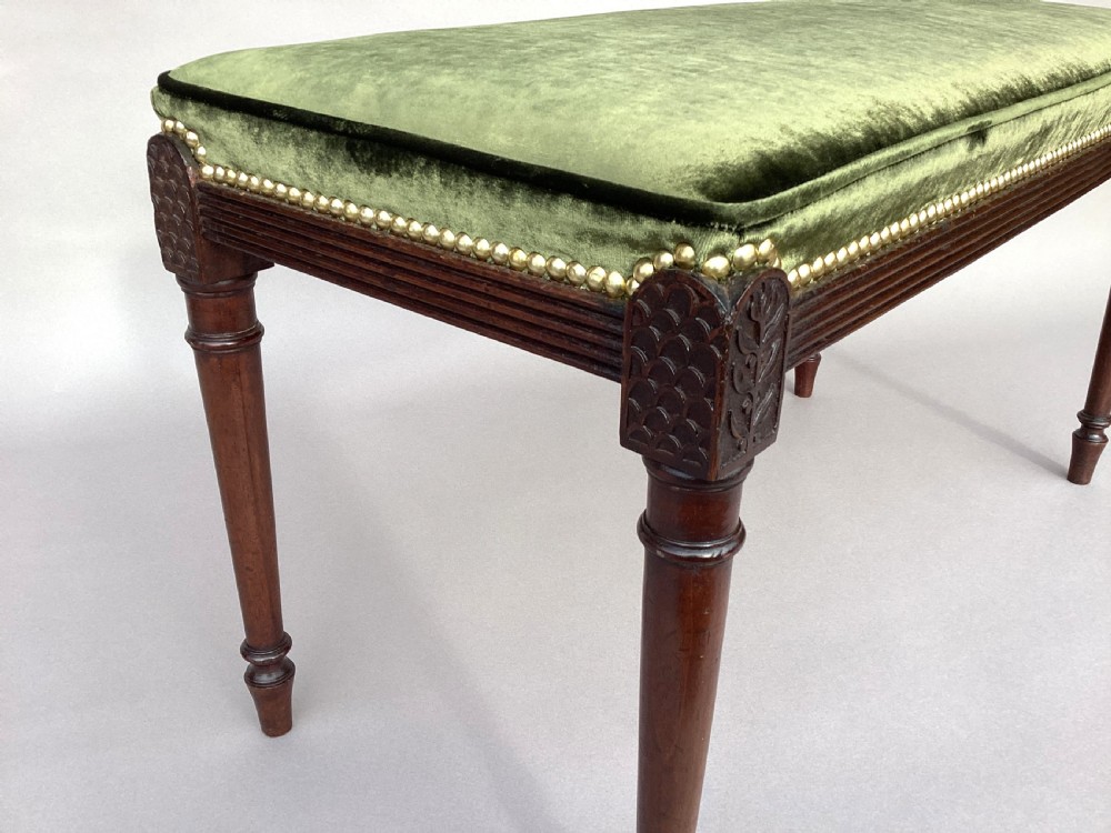 A rectangular George III mahogany window seat featuring sage green velvet upholstery with brass studding, reeded rails, carved corner blocks, and tapered turned legs. View V