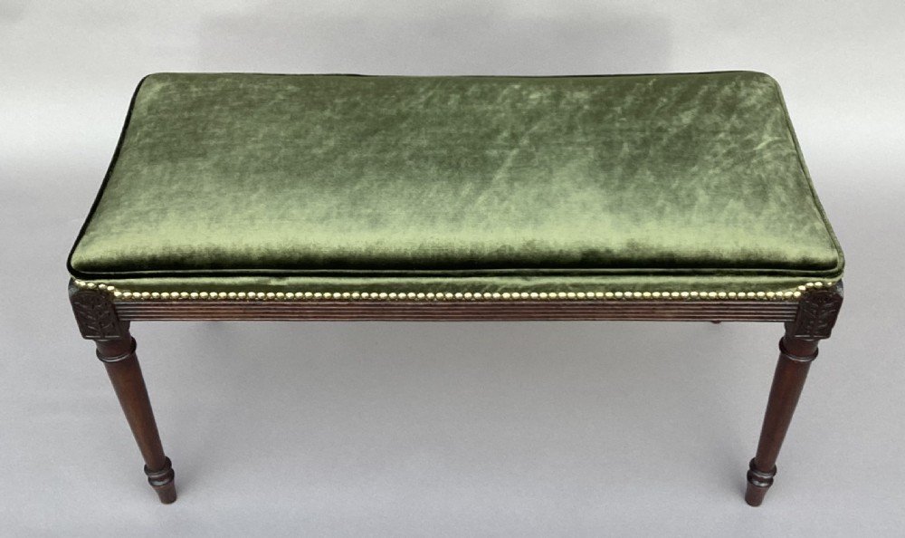 A rectangular George III mahogany window seat featuring sage green velvet upholstery with brass studding, reeded rails, carved corner blocks, and tapered turned legs. View VII