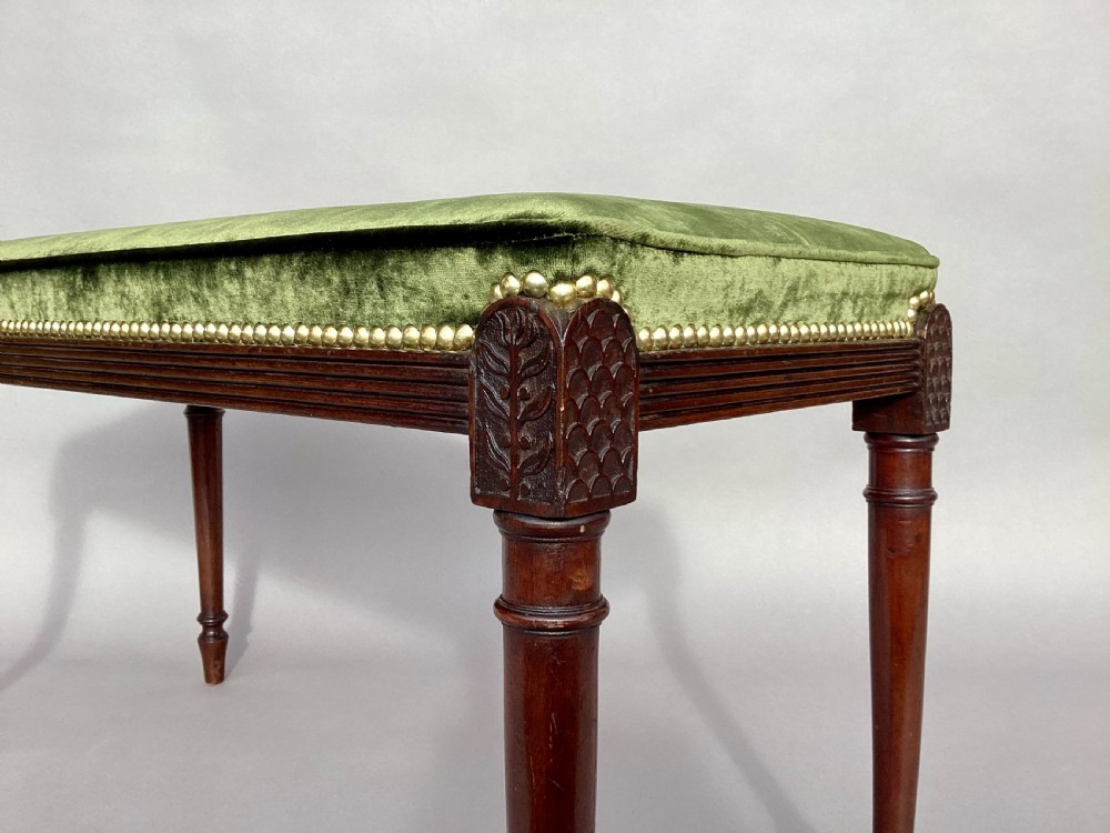 A rectangular George III mahogany window seat featuring sage green velvet upholstery with brass studding, reeded rails, carved corner blocks, and tapered turned legs. View XII