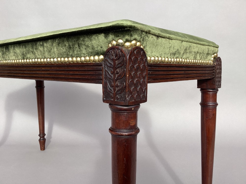 A rectangular George III mahogany window seat featuring sage green velvet upholstery with brass studding, reeded rails, carved corner blocks, and tapered turned legs. View XIII