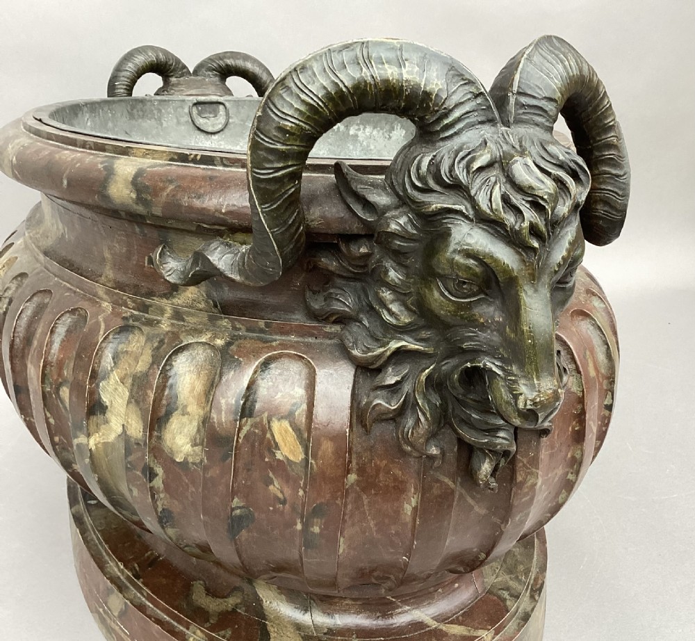 A Regency style oval wine cistern featuring a faux marble painted body with fluted decoration, cast bronze ram head handles, and an internal metal liner. View XVII
