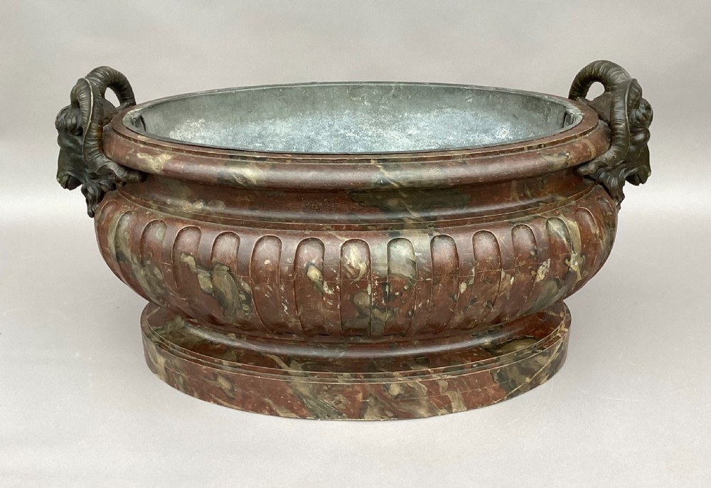 A Regency style oval wine cistern featuring a faux marble painted body with fluted decoration, cast bronze ram head handles, and an internal metal liner. View XXI