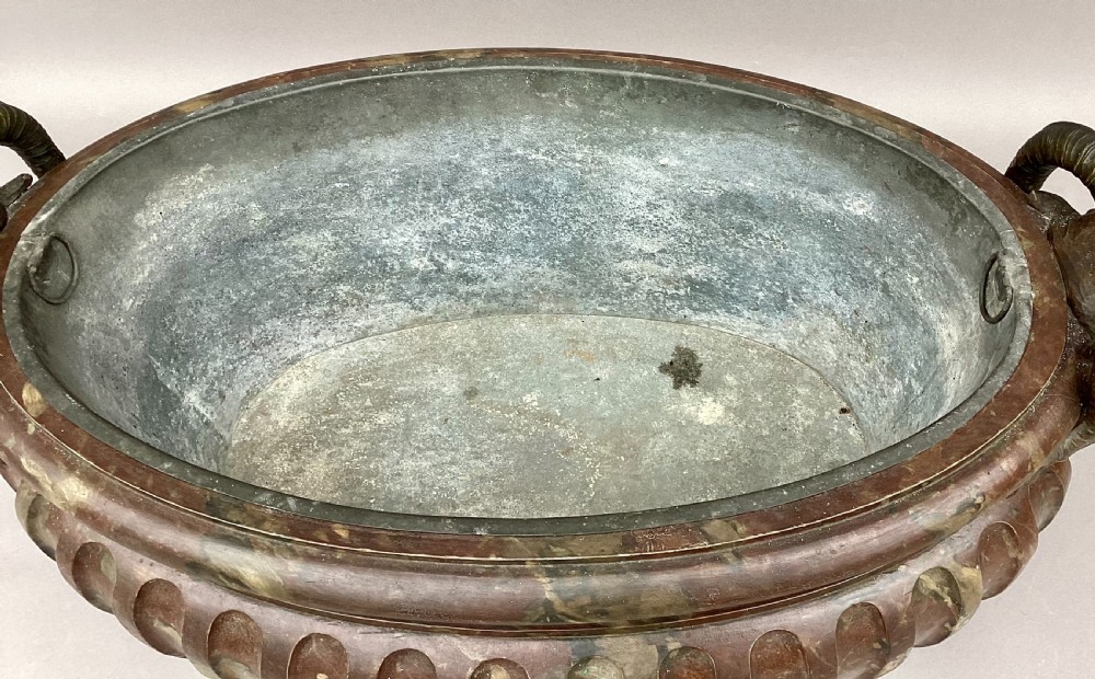 A Regency style oval wine cistern featuring a faux marble painted body with fluted decoration, cast bronze ram head handles, and an internal metal liner. View XXIII