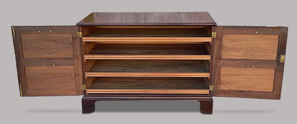 A George III mahogany low press cupboard with doors styled as faux drawers, brass swan-neck handles, bracket feet, and internal sliding shelves. View V