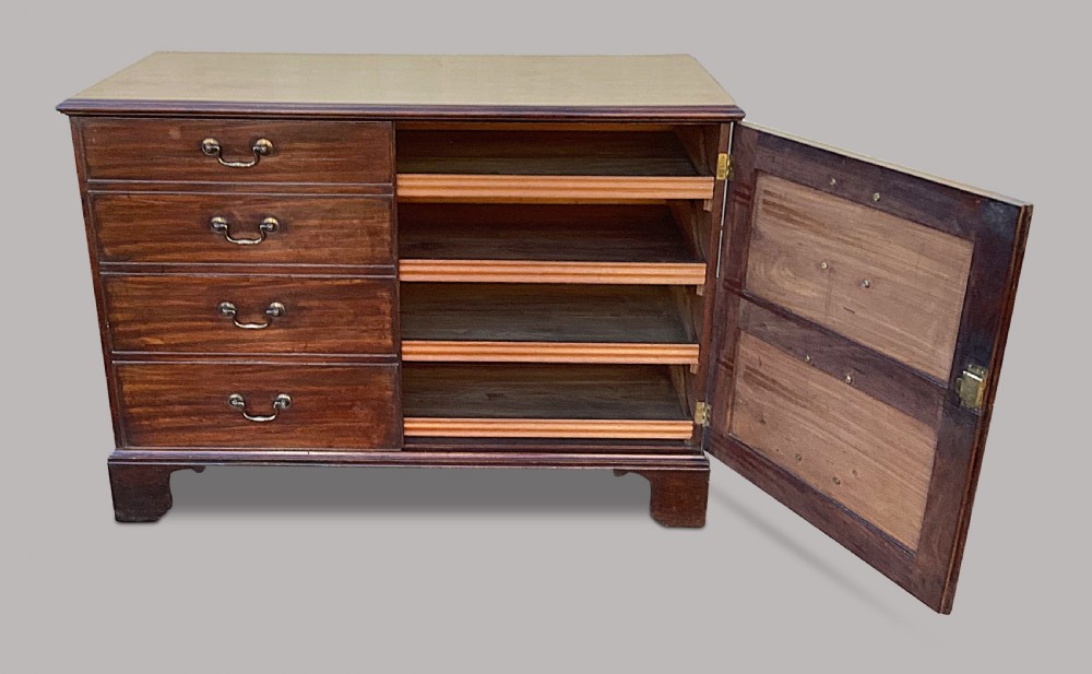 A George III mahogany low press cupboard with doors styled as faux drawers, brass swan-neck handles, bracket feet, and internal sliding shelves. View VI