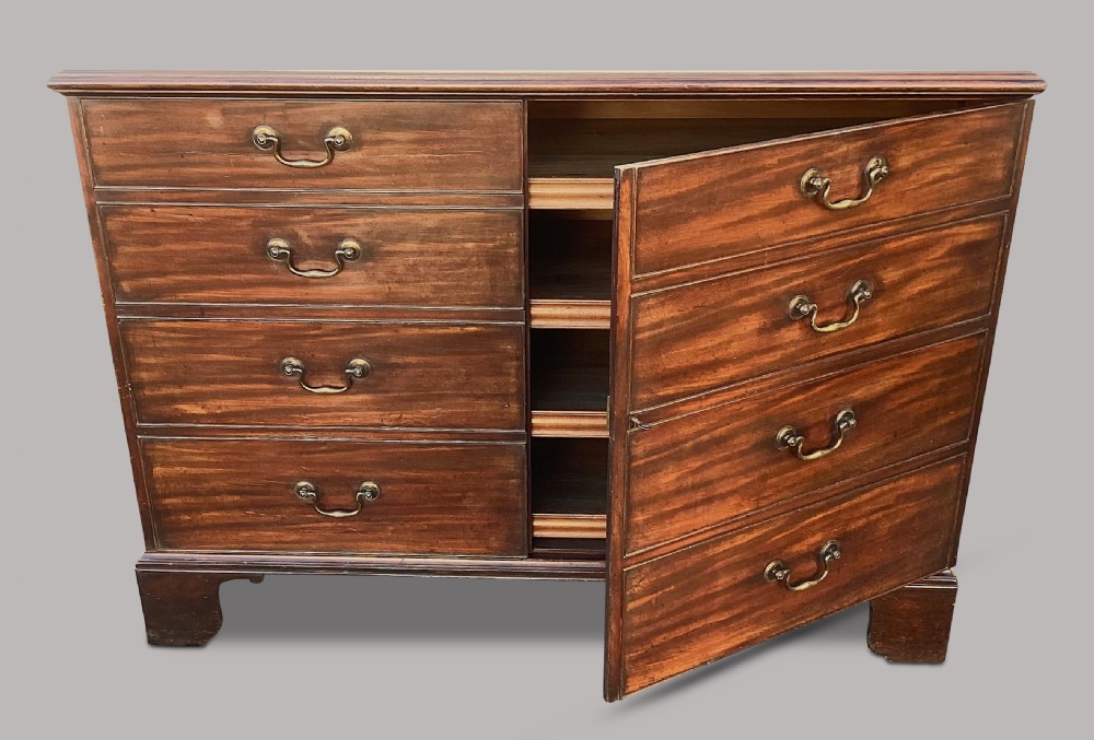A George III mahogany low press cupboard with doors styled as faux drawers, brass swan-neck handles, bracket feet, and internal sliding shelves. View XII