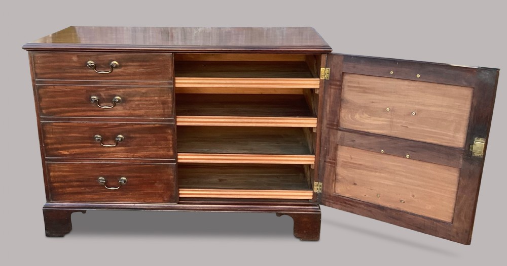 A George III mahogany low press cupboard with doors styled as faux drawers, brass swan-neck handles, bracket feet, and internal sliding shelves. View XVII