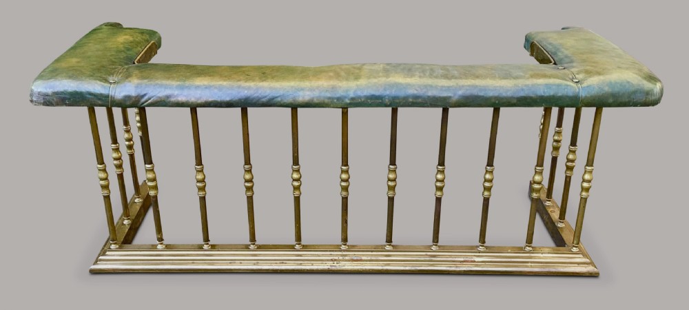 A nineteenth-century brass club fender featuring turned baluster uprights and a continuous U-shaped green leather upholstered seat cushion. View II