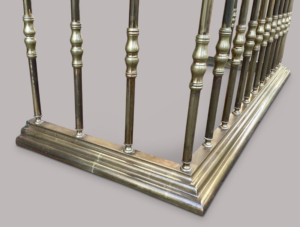 A nineteenth-century brass club fender featuring turned baluster uprights and a continuous U-shaped green leather upholstered seat cushion. View IV