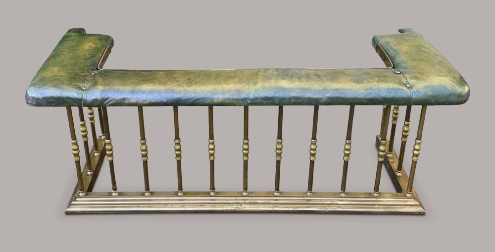 A nineteenth-century brass club fender featuring turned baluster uprights and a continuous U-shaped green leather upholstered seat cushion. View VI