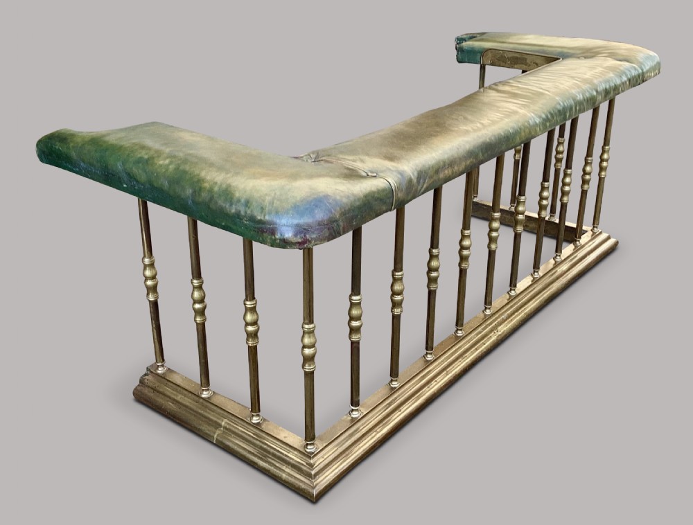 A nineteenth-century brass club fender featuring turned baluster uprights and a continuous U-shaped green leather upholstered seat cushion. View VIII