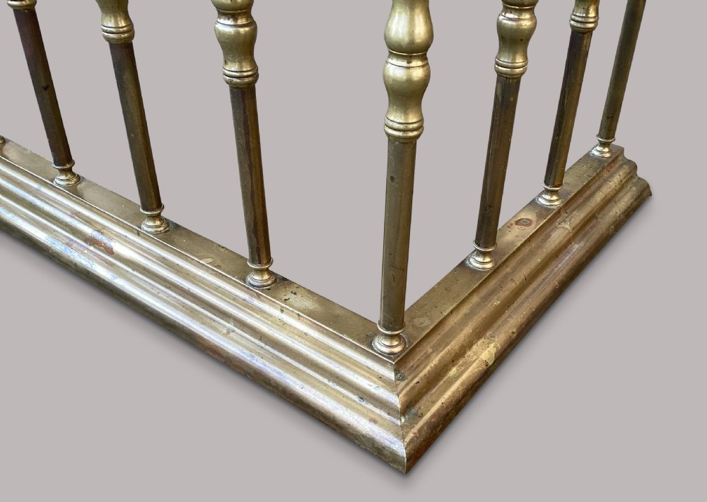 A nineteenth-century brass club fender featuring turned baluster uprights and a continuous U-shaped green leather upholstered seat cushion. View IX