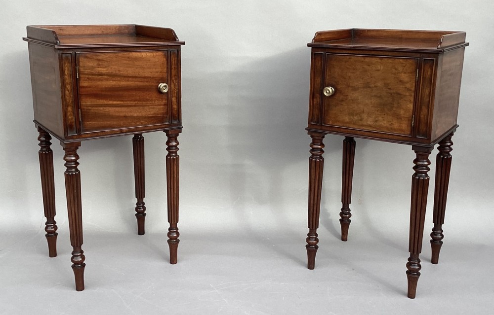 A matched pair of antique Regency mahogany bedside cabinets featuring single door cupboards, low gallery tops, round brass handles, and slender reeded turned legs. View II