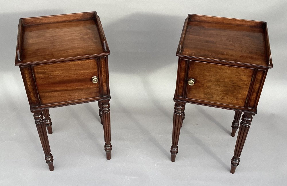 A matched pair of antique Regency mahogany bedside cabinets featuring single door cupboards, low gallery tops, round brass handles, and slender reeded turned legs. View XIX