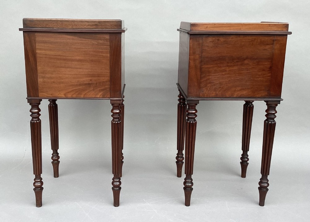 A matched pair of antique Regency mahogany bedside cabinets featuring single door cupboards, low gallery tops, round brass handles, and slender reeded turned legs. View XX