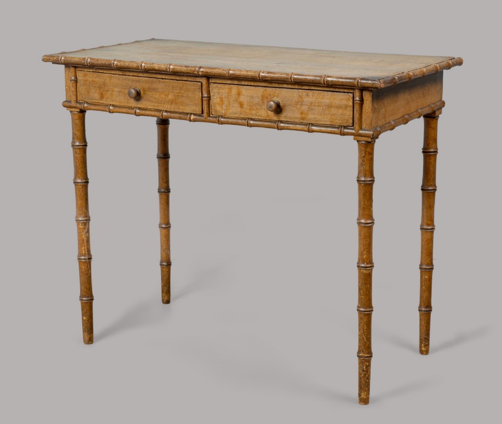 A Regency era side table crafted with turned faux bamboo legs, two drawers with round wooden knobs, and an original painted ochre finish.