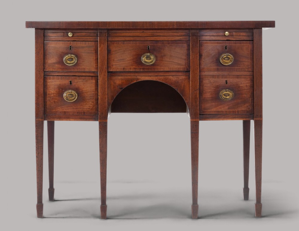 A George III mahogany bow-fronted sideboard featuring brass oval handles, drawer compartments, an arched central apron, and square tapered legs.