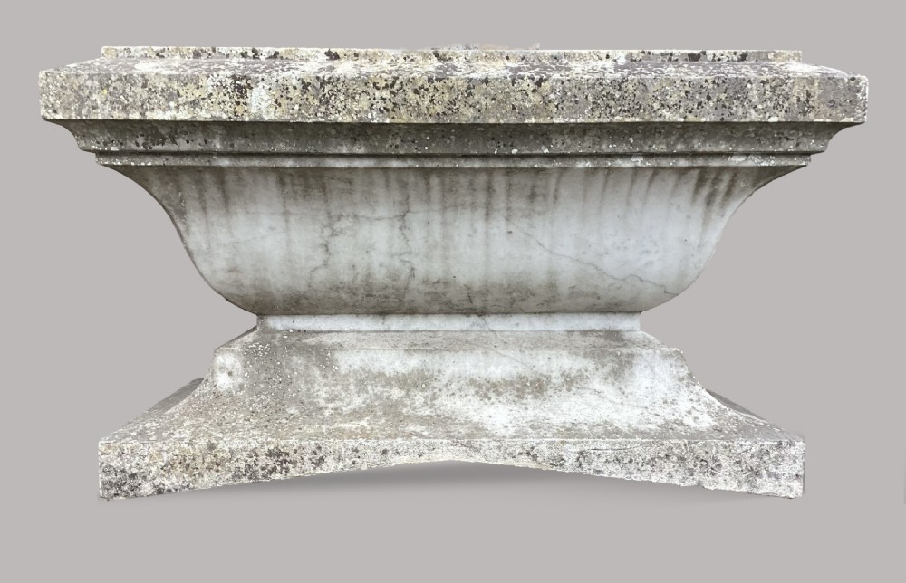 A late 18th-century Neoclassical Carrara marble cistern featuring a curved basin, flared top rim moulding, and a stepped rectangular base with a weathered stone patina.