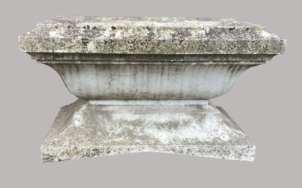 A late 18th-century Neoclassical Carrara marble cistern featuring a curved basin, flared top rim moulding, and a stepped rectangular base with a weathered stone patina. View V