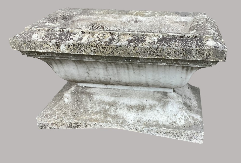 A late 18th-century Neoclassical Carrara marble cistern featuring a curved basin, flared top rim moulding, and a stepped rectangular base with a weathered stone patina. View VII