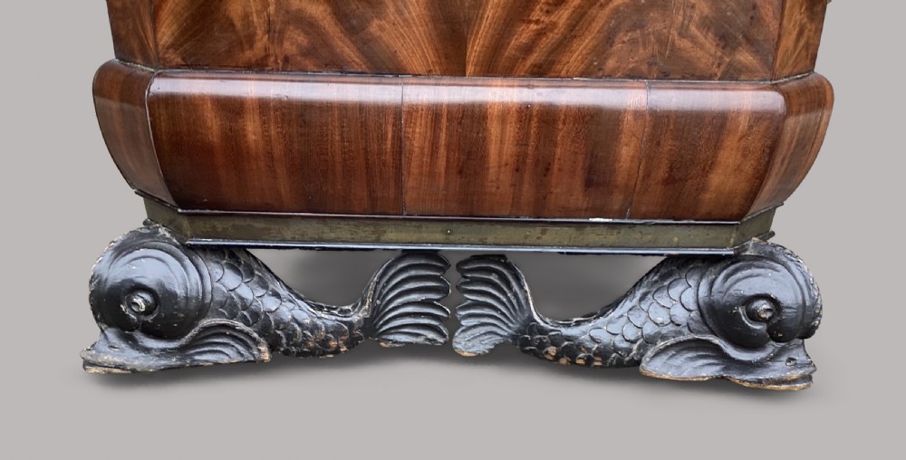 A Regency period mahogany wine cellarette of sarcophagus form featuring brass banding, carrying handles, and carved dolphin feet. View III