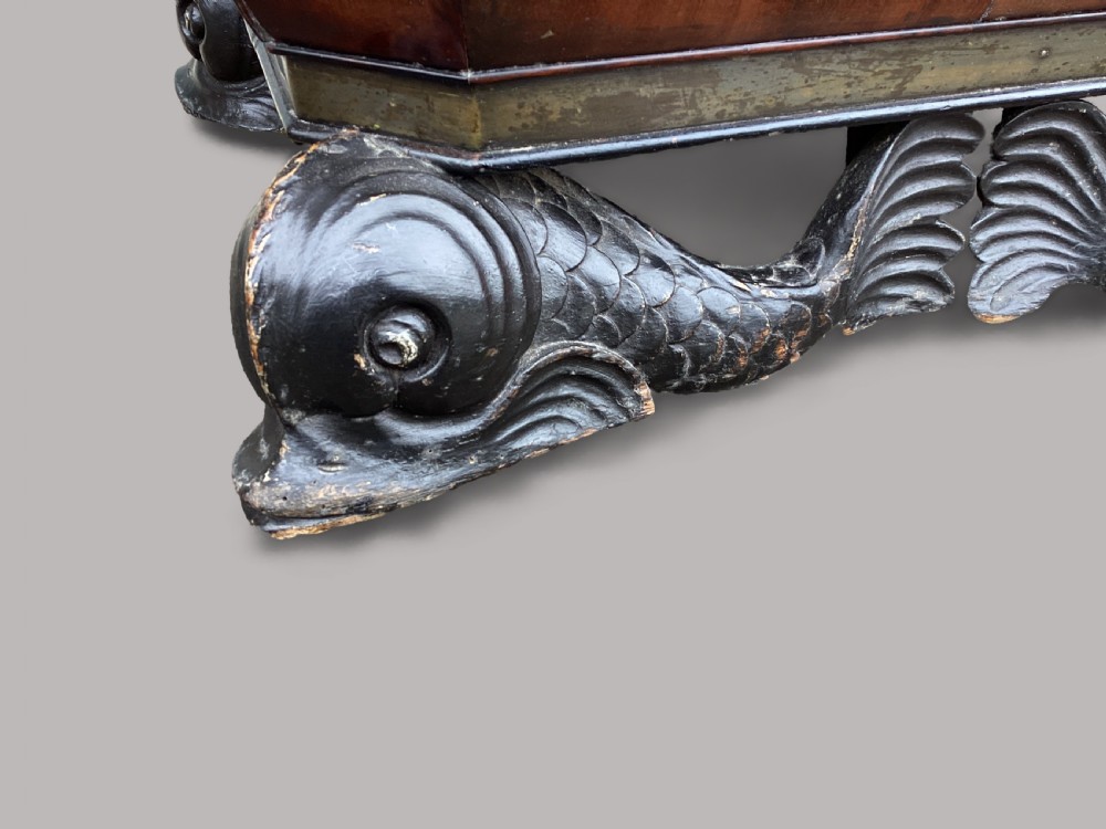 A Regency period mahogany wine cellarette of sarcophagus form featuring brass banding, carrying handles, and carved dolphin feet. View VIII
