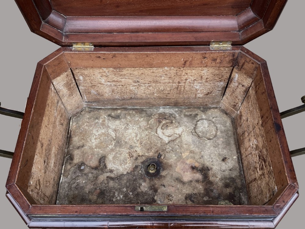 A Regency period mahogany wine cellarette of sarcophagus form featuring brass banding, carrying handles, and carved dolphin feet. View IX