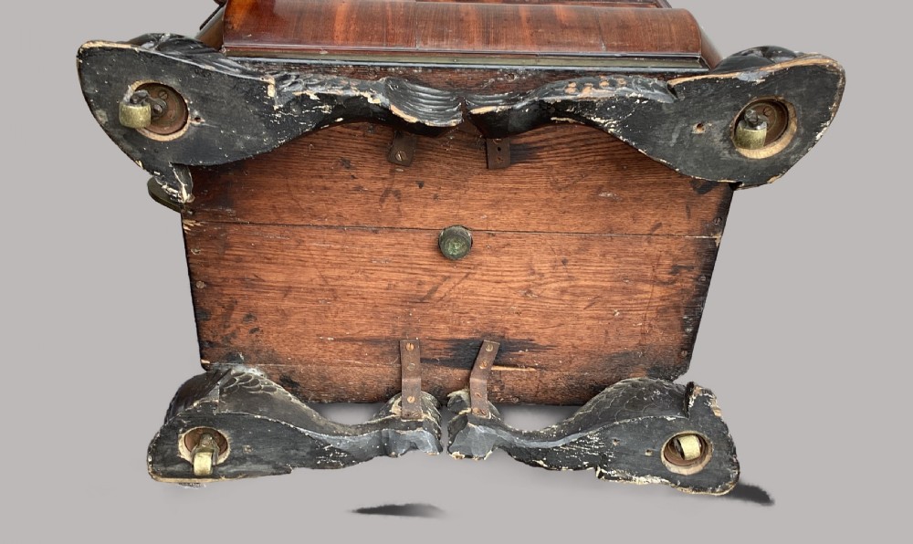 A Regency period mahogany wine cellarette of sarcophagus form featuring brass banding, carrying handles, and carved dolphin feet. View X