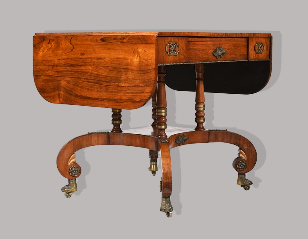 A Regency period rosewood drop-leaf sofa table featuring frieze drawers, turned columns, gilt brass mounts, and splayed legs with brass castors. View II
