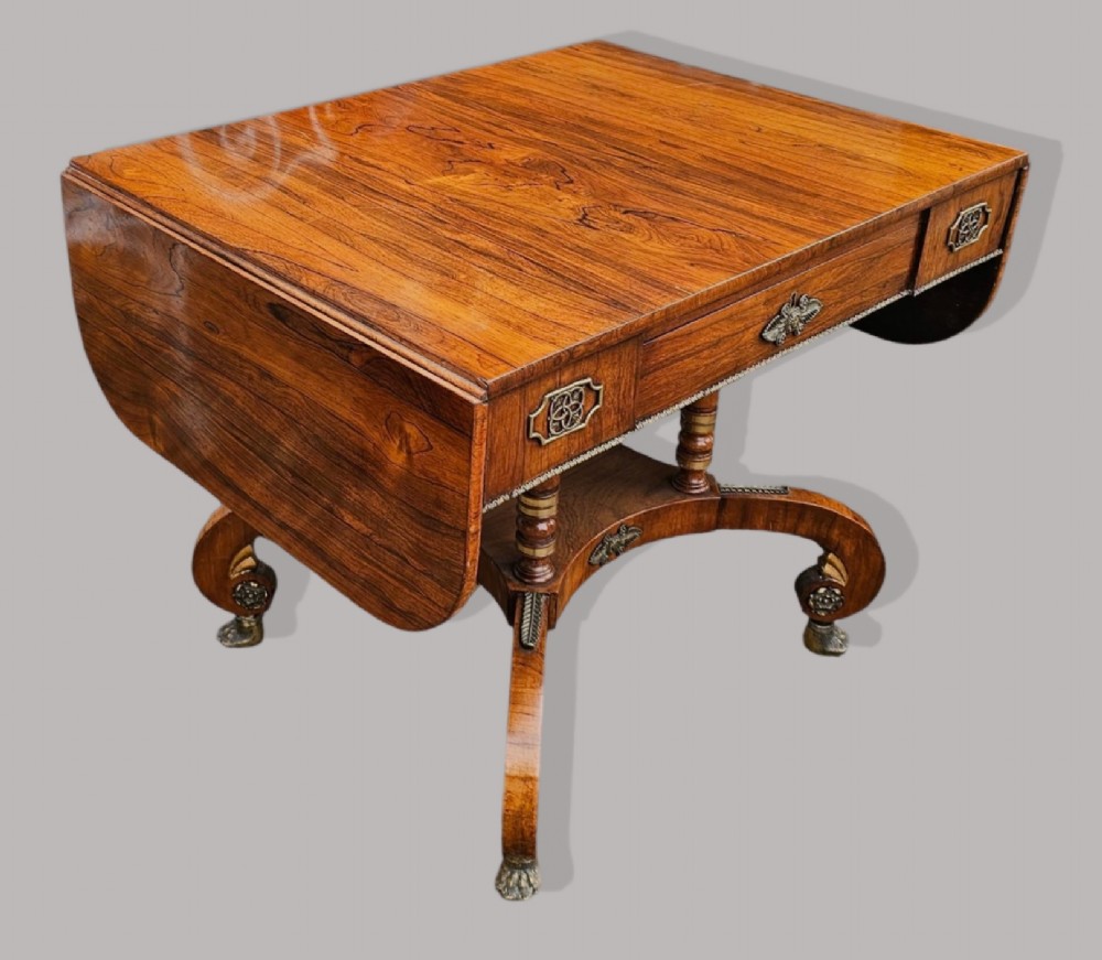 A Regency period rosewood drop-leaf sofa table featuring frieze drawers, turned columns, gilt brass mounts, and splayed legs with brass castors. View VII