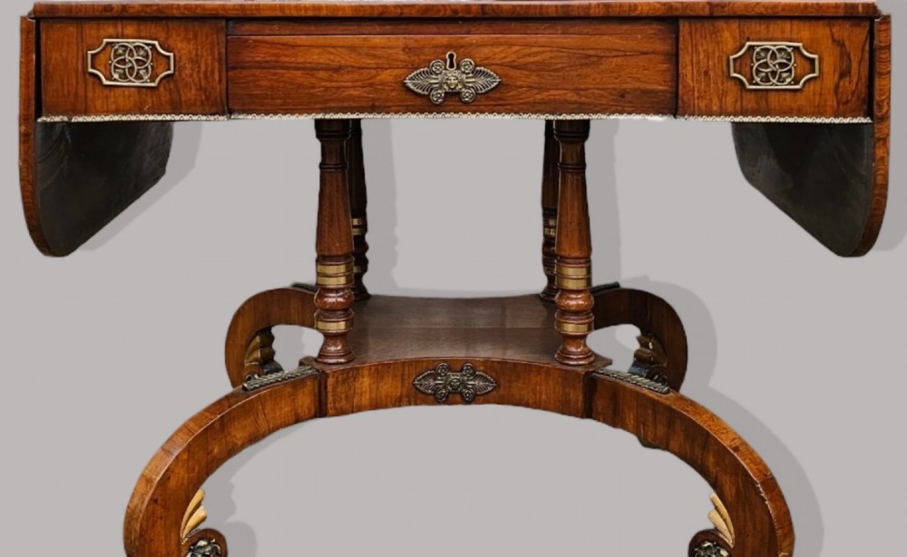 A Regency period rosewood drop-leaf sofa table featuring frieze drawers, turned columns, gilt brass mounts, and splayed legs with brass castors. View IX