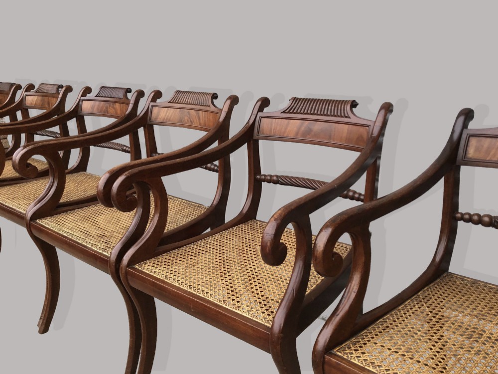 A set of six Regency mahogany open armchairs featuring woven cane seats, curved scroll arms, reeded top rails, and sabre legs. View II