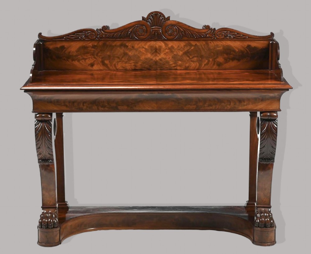 A Regency mahogany console table featuring a carved scroll cresting backboard, flame mahogany veneers, carved acanthus leaf legs, and paw feet on a plinth base.
