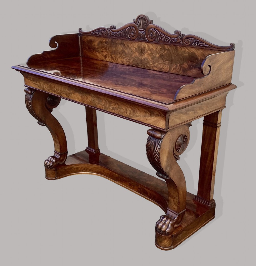 A Regency mahogany console table featuring a carved scroll cresting backboard, flame mahogany veneers, carved acanthus leaf legs, and paw feet on a plinth base. View II