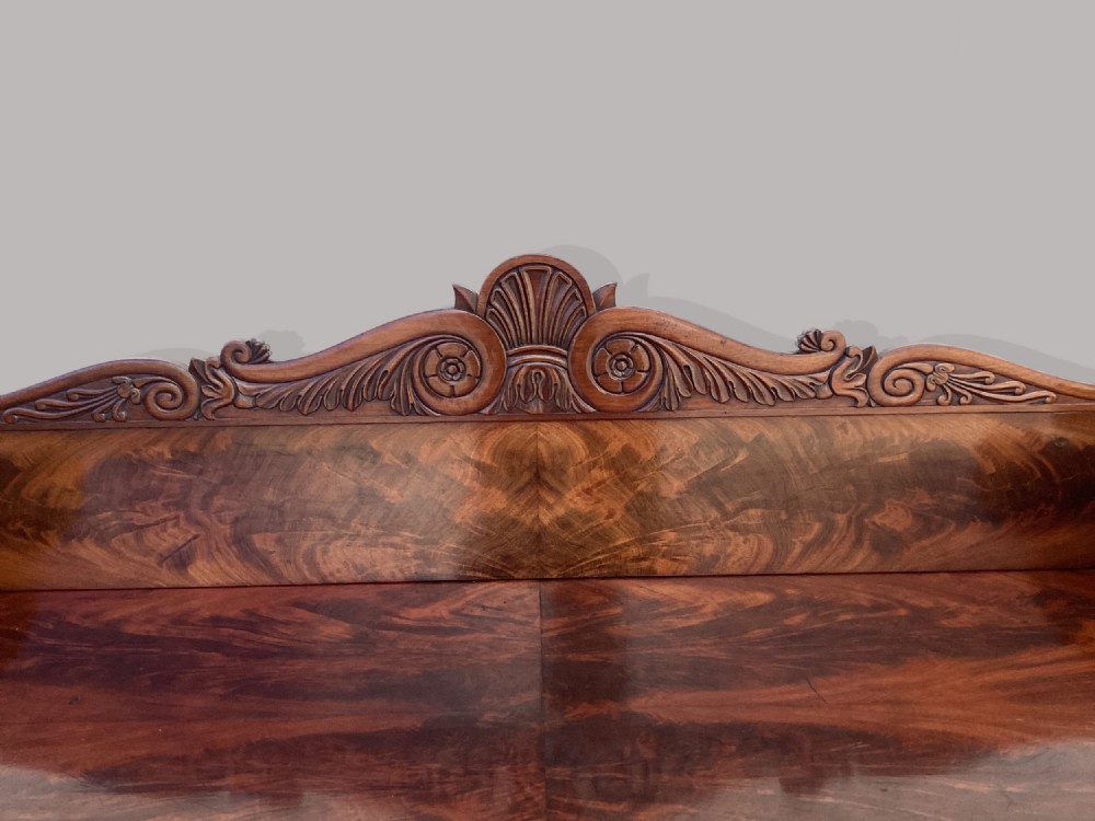A Regency mahogany console table featuring a carved scroll cresting backboard, flame mahogany veneers, carved acanthus leaf legs, and paw feet on a plinth base. View V