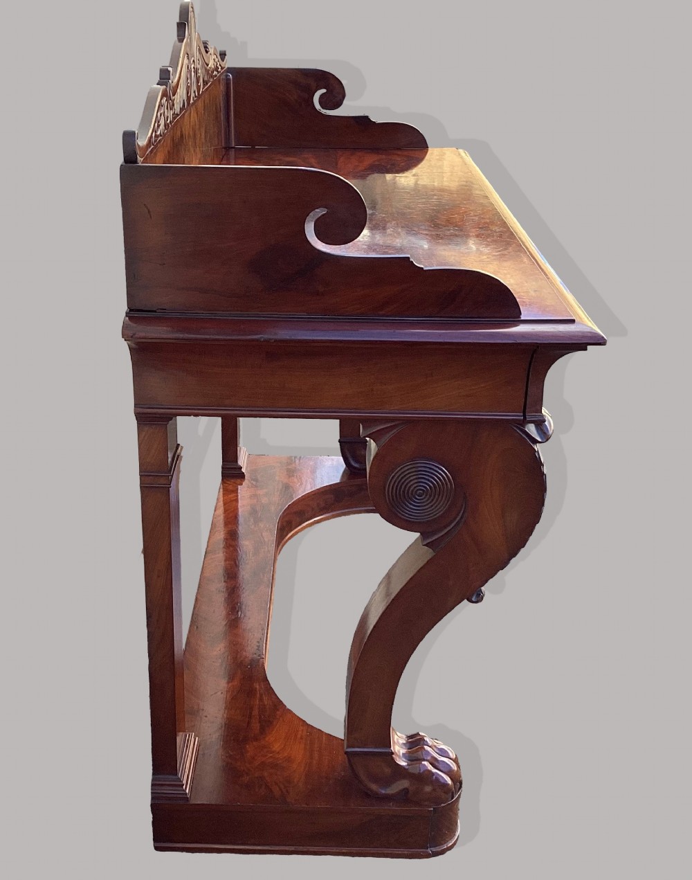 A Regency mahogany console table featuring a carved scroll cresting backboard, flame mahogany veneers, carved acanthus leaf legs, and paw feet on a plinth base. View XII