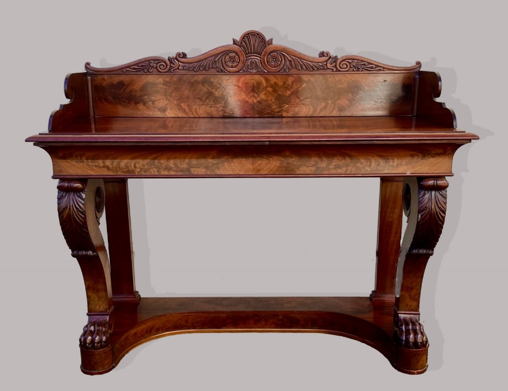 A Regency mahogany console table featuring a carved scroll cresting backboard, flame mahogany veneers, carved acanthus leaf legs, and paw feet on a plinth base. View XIII