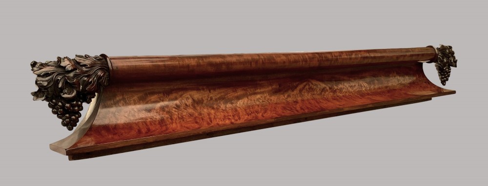 A long George IV figured mahogany pelmet featuring carved acanthus leaves and grape cluster finials at either end.