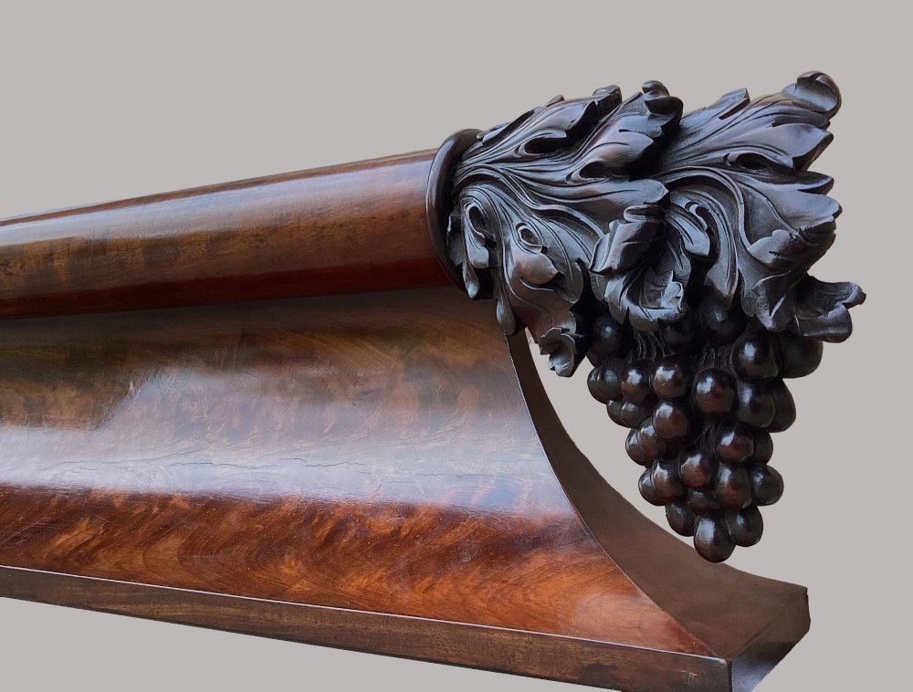 A long George IV figured mahogany pelmet featuring carved acanthus leaves and grape cluster finials at either end. View X