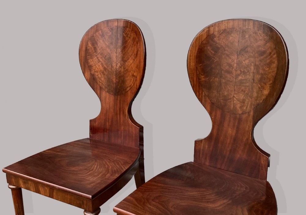A set of six George III mahogany hall chairs featuring rounded cartouche-shaped backrests, solid wooden seats, and turned front legs. View VI