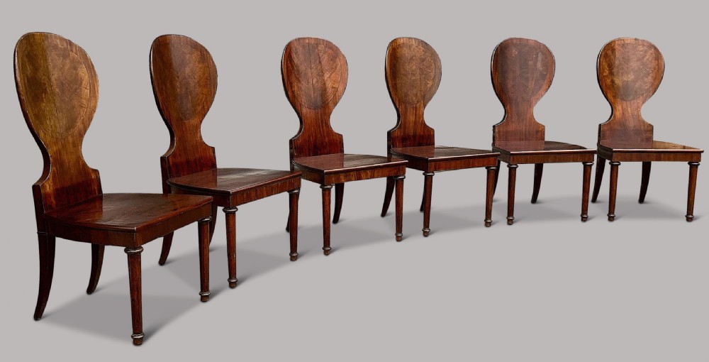 A set of six George III mahogany hall chairs featuring rounded cartouche-shaped backrests, solid wooden seats, and turned front legs. View VII