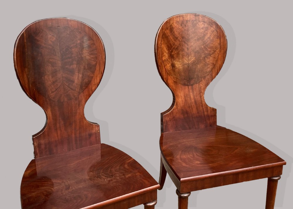 A set of six George III mahogany hall chairs featuring rounded cartouche-shaped backrests, solid wooden seats, and turned front legs. View XII