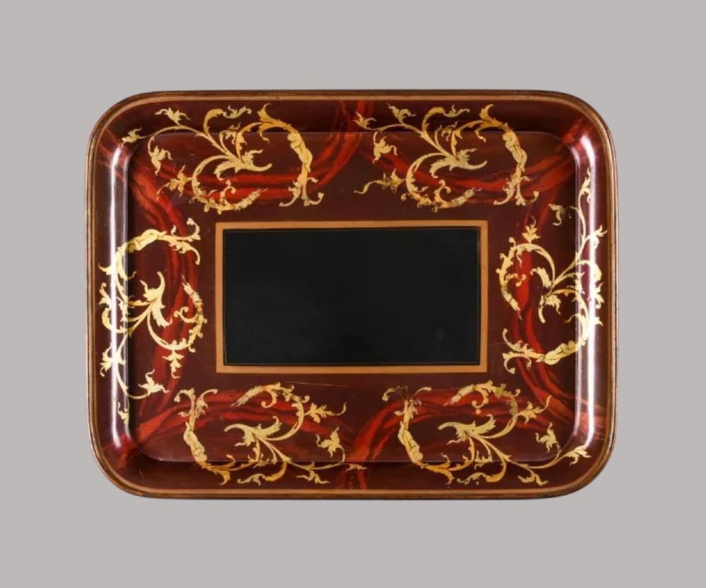 A rectangular Regency papier-mache tray with rounded edges, featuring gilded foliage and red swirl decoration surrounding a central black panel.