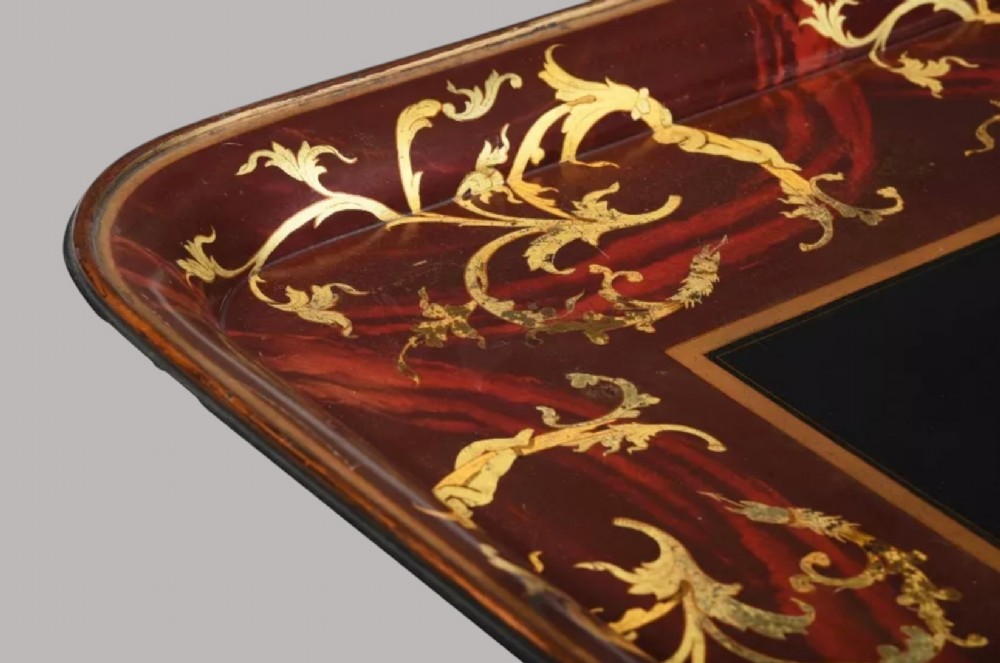 A rectangular Regency papier-mache tray with rounded edges, featuring gilded foliage and red swirl decoration surrounding a central black panel. View III