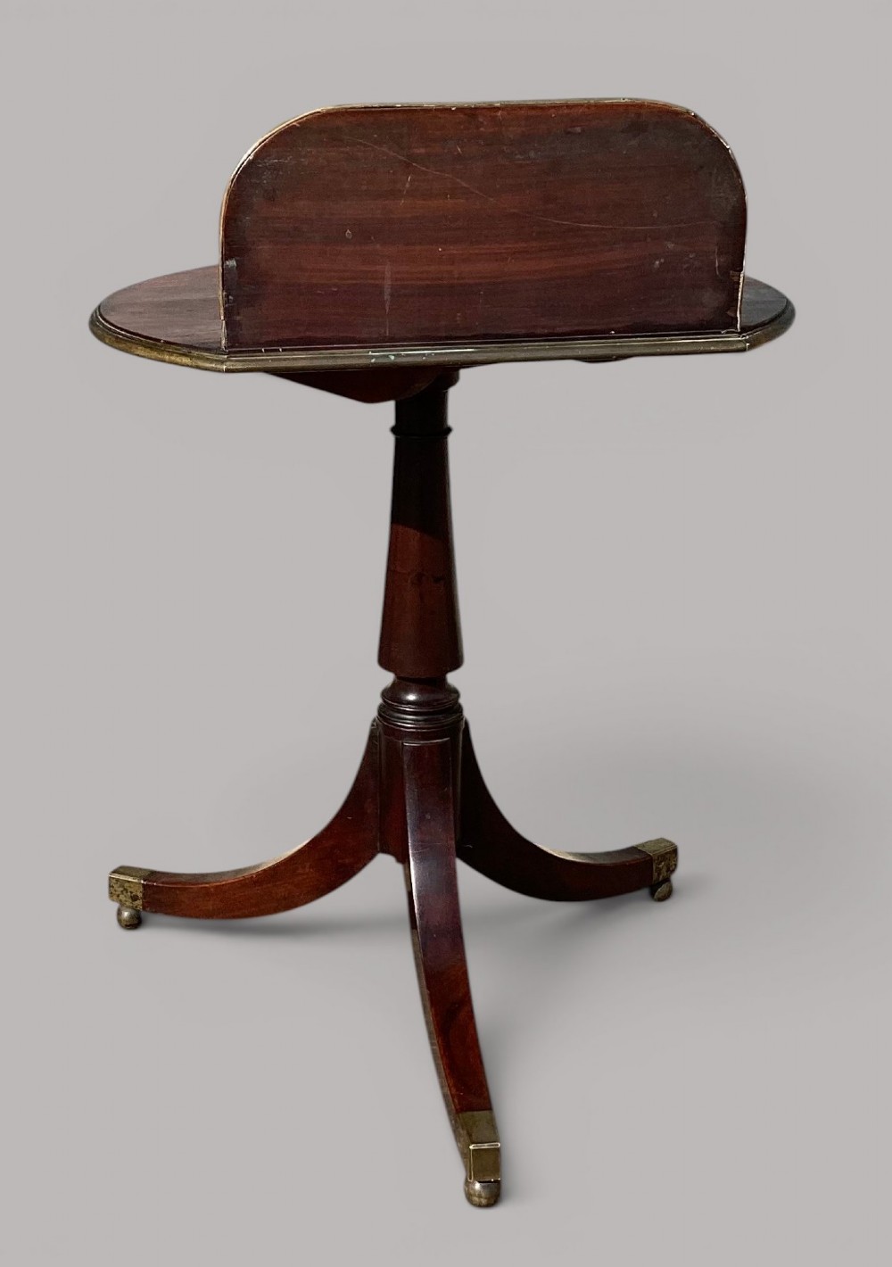 A George III mahogany tripod occasional table featuring a raised back panel, brass moulding on the circular top, a turned central column, and three curved legs ending in brass caps. View IV