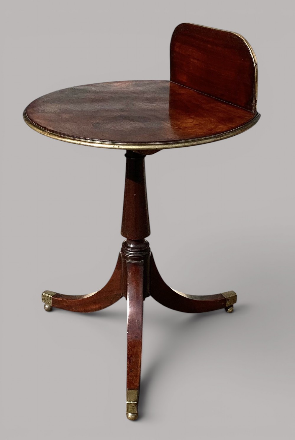 A George III mahogany tripod occasional table featuring a raised back panel, brass moulding on the circular top, a turned central column, and three curved legs ending in brass caps. View VIII