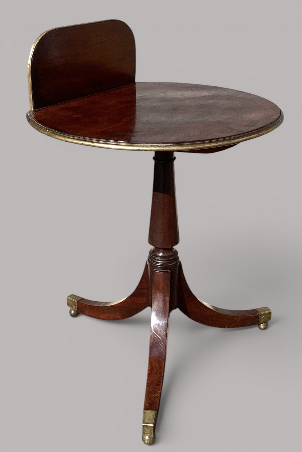 A George III mahogany tripod occasional table featuring a raised back panel, brass moulding on the circular top, a turned central column, and three curved legs ending in brass caps. View IX