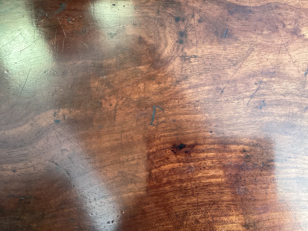 A George III mahogany tripod occasional table featuring a raised back panel, brass moulding on the circular top, a turned central column, and three curved legs ending in brass caps. View X