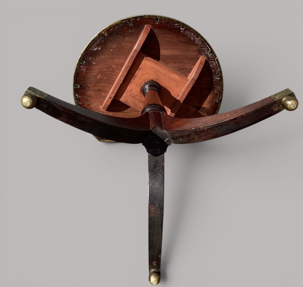 A George III mahogany tripod occasional table featuring a raised back panel, brass moulding on the circular top, a turned central column, and three curved legs ending in brass caps. View XI